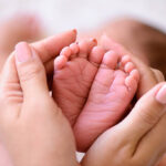 Mother holding tiny foot of newborn baby