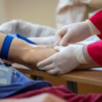 Medical professional drawing blood from donor's arm in a clinical setting.