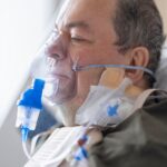 A senior adult patient using an oxygen mask in a hospital setting for medical care.