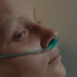 Close-up of a woman lying in a hospital bed with nasal cannula oxygen support.