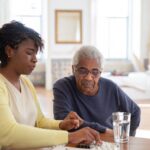 Nurse helping senior man with his medication at home, ensuring health and safety.
